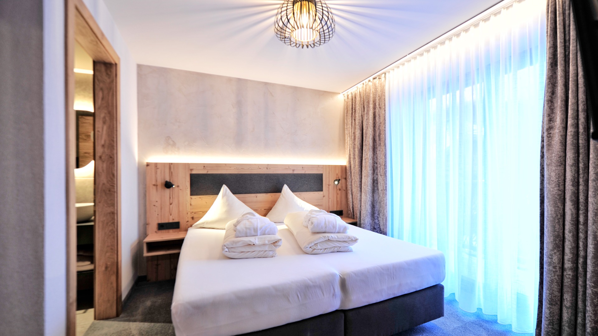 Helles Schlafzimmer mit Doppelbett, Vorhängen, gemütlicher Beleuchtung und modernem Holz-Design.