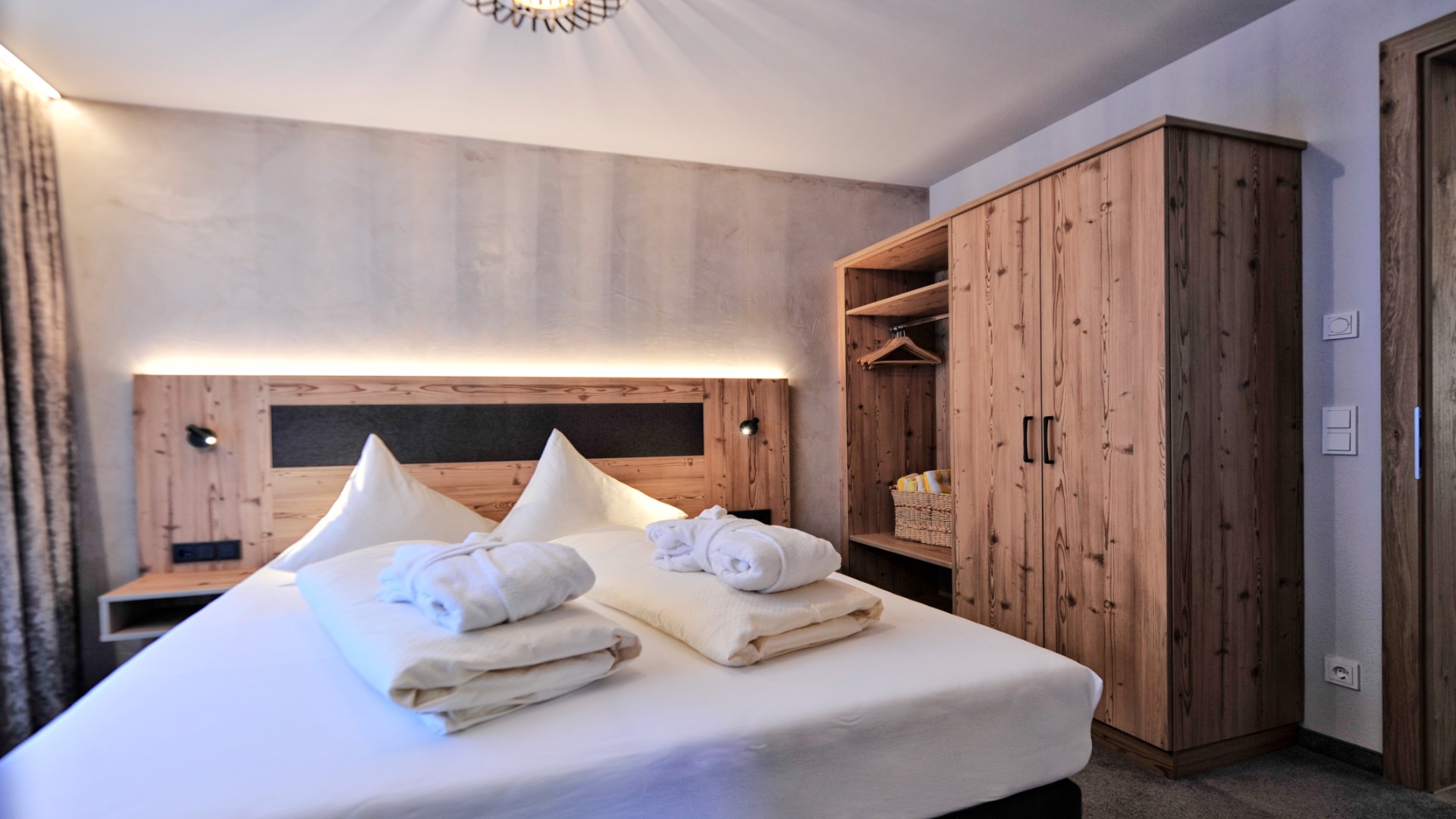 Schlafzimmer mit Doppelbett, Holzkleiderschrank, Nachttischen und gedämpfter Wandbeleuchtung.